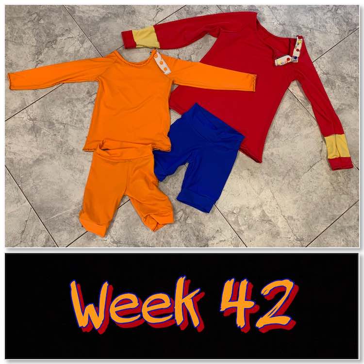 Image shows the finished swim garments laid out on the kitchen floor with a black rectangle below showing the words "week 42" in orange and red. The swim garments are composed of an orange rash guard, orange shorts, red rash guard with yellow bands, and blue shirts.