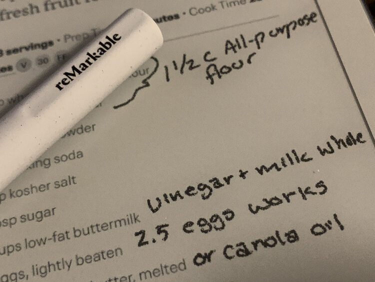 Image shows a closeup view of the reMarkable showing the logo on the pen, laid over top of the device, and the text I wrote over the template.