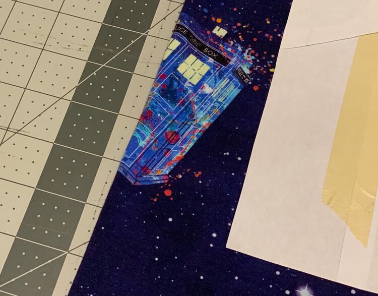Image shows the TARDIS panel folded in half over the cutting board. The pattern piece is wrong side up and off to the side so you can see the TARDIS.