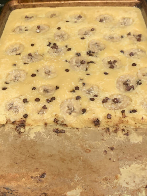 The baked pan of pancakes is now show but the first third has been dished showing the inner side of the sheet pan pancakes and the remnants left behind when you dish. 