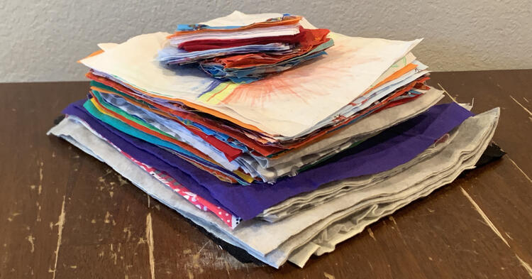 Image shows a stack of fabric squares with smaller rectangles on top. The larger ones squares are at the bottom with the small rectangles on top of the smaller squares of fabric.