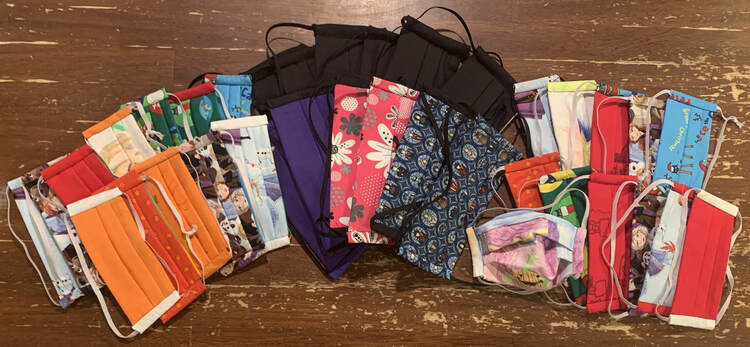 Image shows an array of masks laid out on the table. In the center back are Matt's black ones with mine overlapping. To the left are Zoey's and Ada's are to the right.