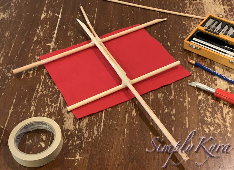 Image shows all the parts of the mast taped together and laid overtop of the sail on the table. You can see tape at all the join points.