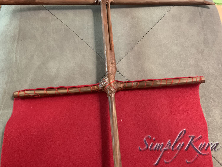 Image shows the mast with the smaller horizontal mast in the center. At the top you can see a bit of the upper horizontal mast. From the bottom horizontal mast you can see the felt laid out beneath the mast and the bright red thread wrapping the top around the mast.
