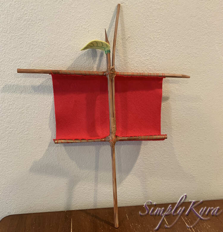 Image shows the sail now upright on the table and leaning against the wall. From this angle the sail balloons towards the wall and can see the red threads that sewed the sail on.