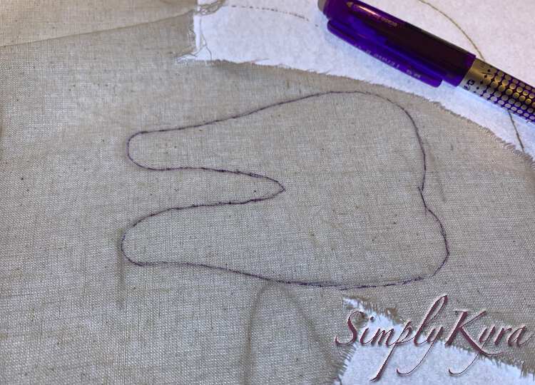 Image shows a blue inked tooth on white fabric with the paper and then turned on lightbox underneath it. The blue disappearing ink pen is laid out beside the fabric. 