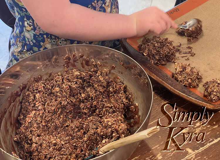 Image shows Ada's arm as she uses a spoon to make another cookie next to three others on a Silpat lined baking sheet. Beside it sits a metal bowl filled with the rest of the no-bake dough.