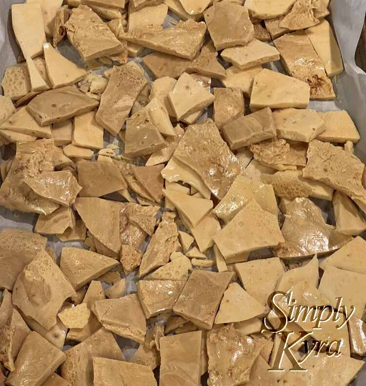 Image shows a parchment lined cookie sheet full of sharp pieces of honeycomb candy in two shades.