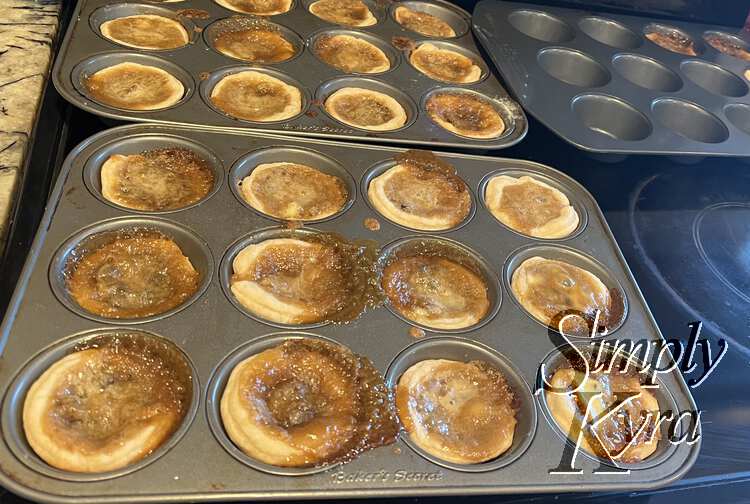 Image shows the three muffin tins resting on the oven top with browned, bubbled, tarts resting inside to col.