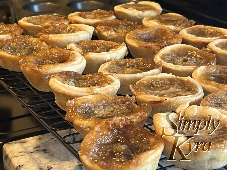 Image is a closeup of a cooling rack filled with browned and yummy butter tarts.