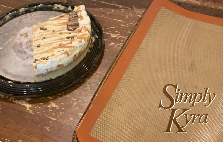 Image shows a Silpat lined cookie sheet to the right and a partially eaten, only five pieces left, decorated cheesecake to the left.