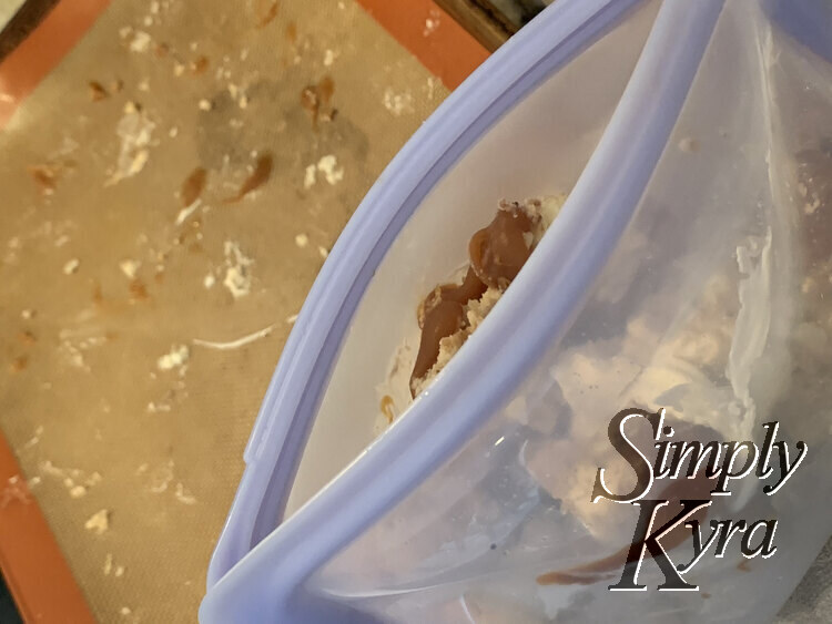 Image shows a light blue Stasher bag filled with cheesecake balls and open at the top. The brown and white dirtied Silpat liner is seen in the background.