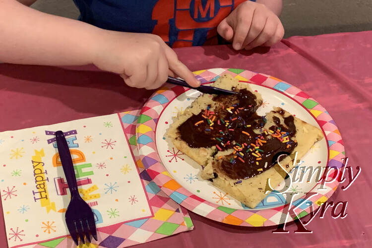 Image shows Ada cutting into a pancake coated in Nutella and rainbow sprinkles. It's sitting on a happy birthday plate next to a napkin. Leftovers from her party stuff.