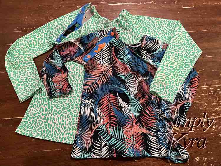Image shows the two new long sleeved tops with a matching shark-themed plackard on the one shoulder. The shirt behind is green cheetah spots while the one in front is colorful palm leaves. 