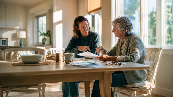 Mother and daughter reviewing IHSS paperwork with a LiveWell caregiver at a kitchen table in a warm Los Angeles home.