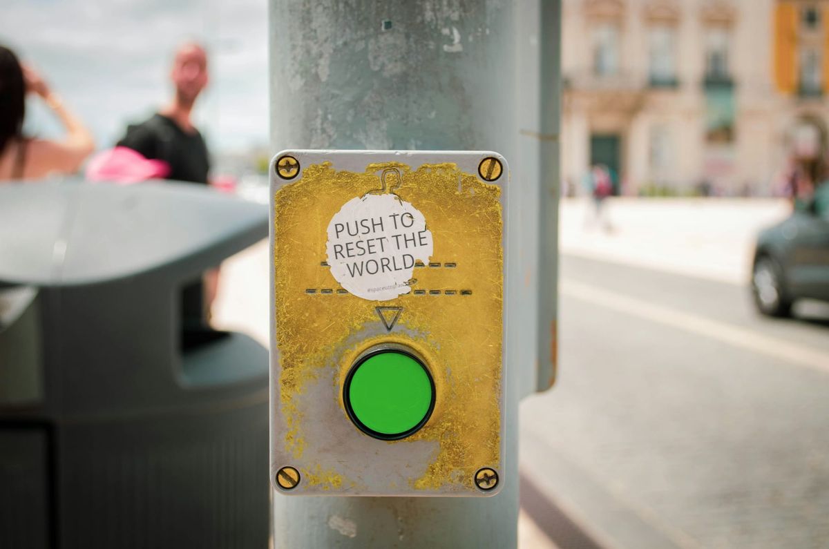 Picture of a stoplight in Lisbon. Sticker "Push to reset the world" 