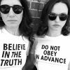 Photo of two women, wearing t-shirts saying "Believe in the truth" and "Do not obey in advance"