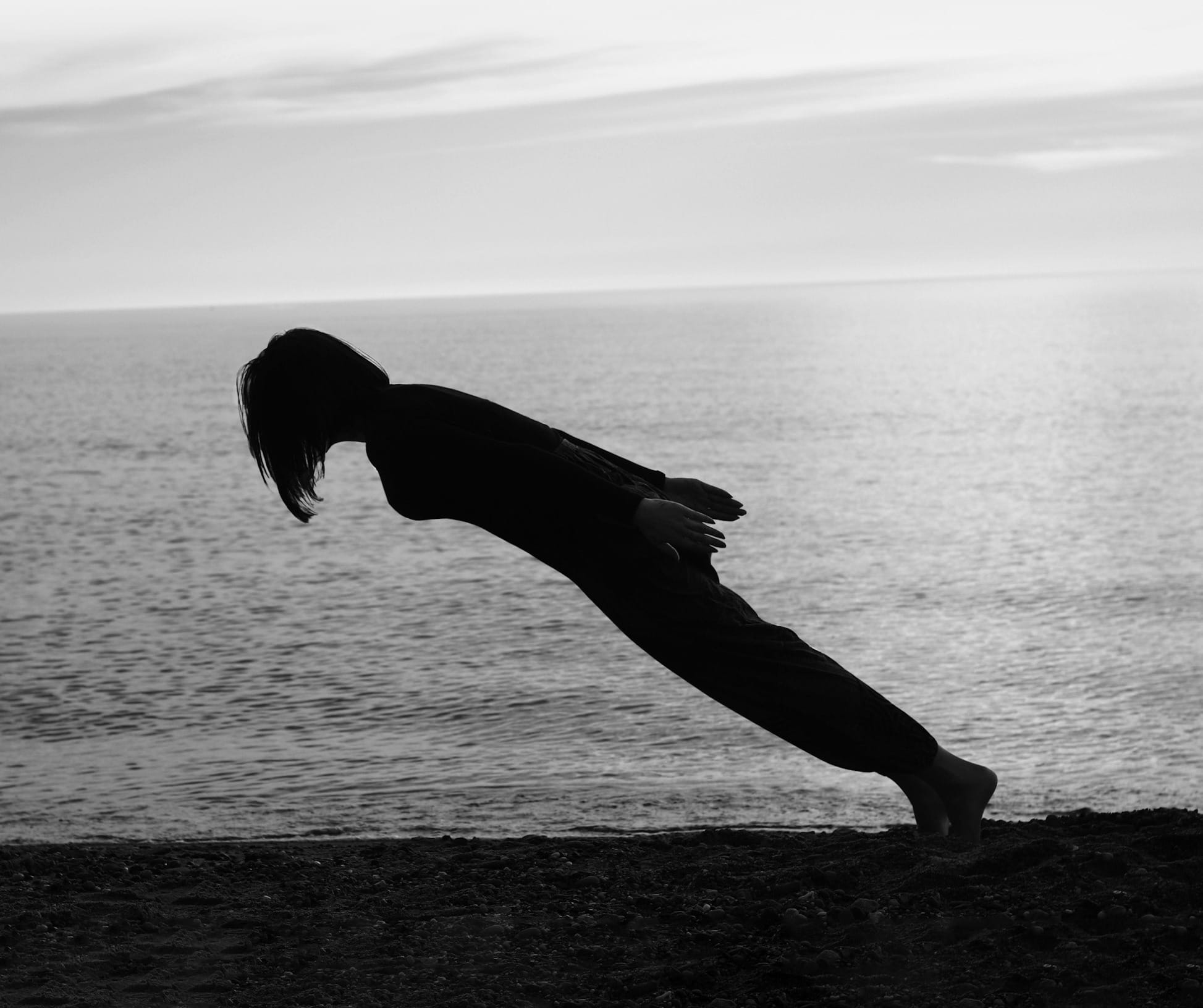 Silhouette of a woman on the shore leaning forward, her posture demonstrating the pull and effect of gravity.