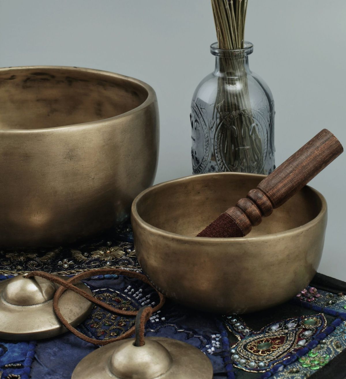 A brass singing bowl with a wooden mallet, cymbals, and a glass fragrance bottle—representing the sacred stillness, sound, and soul of manifestation practice