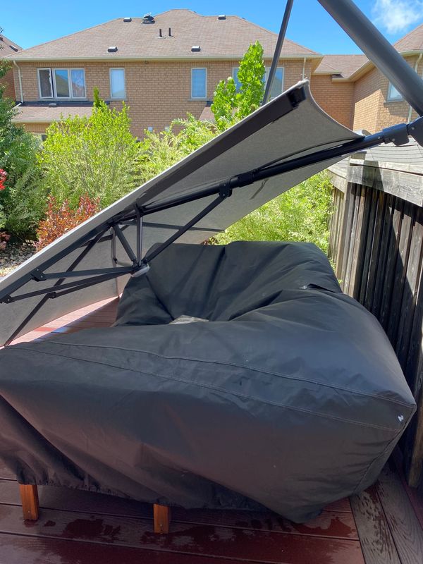 A quiet backyard with overgrown trees and a fallen patio umbrella resting near the glass door, hinting at a recent gust of wind and unsettled stillness.