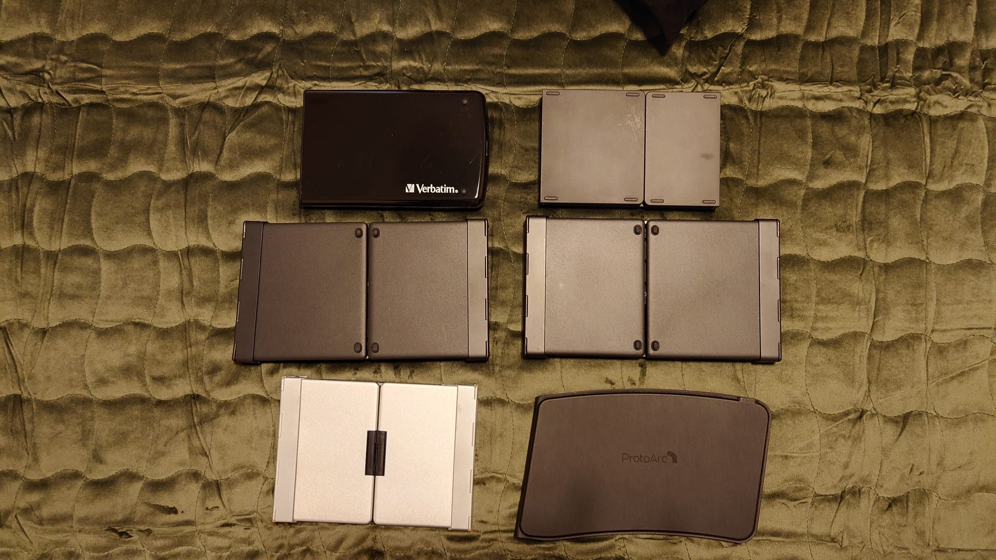 Six Bluetooth keyboards folded up laying on a green velvety background - my BT KB collection