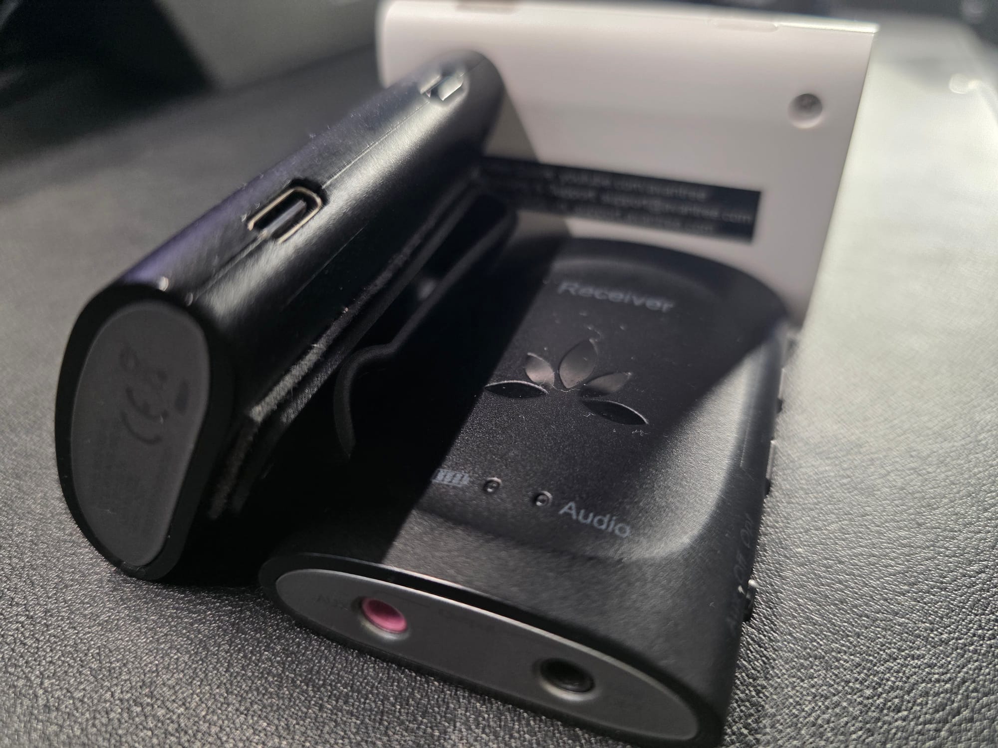 The Avantree kit lying on a black desk.  One receiver is on its side and the other is on its back.  The transmitter has its back side showing. The Avantree receivers are black and the transmitter is white.