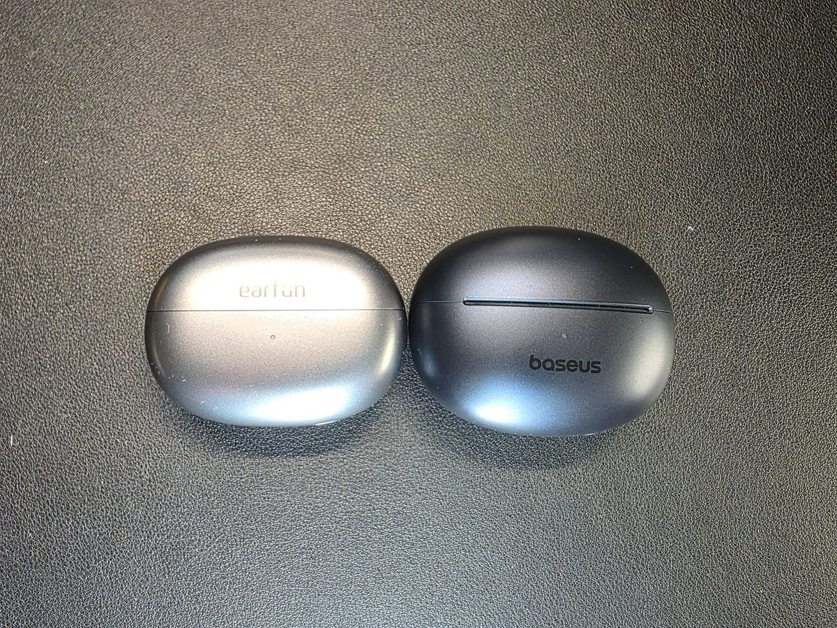 The EarFun Clip are shown in their closed gray case on the left and the Baseus Bowie MC1 Pro in its closed charcoal case on the right