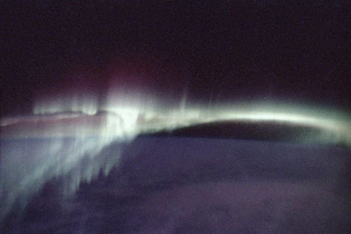 grainy purple field with a bright pale green trail across the middle. aurora borealis from spacelab