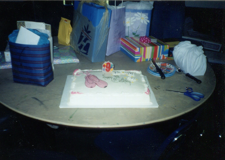 overexposed phot of a birthday cake surrounded by presents on a table