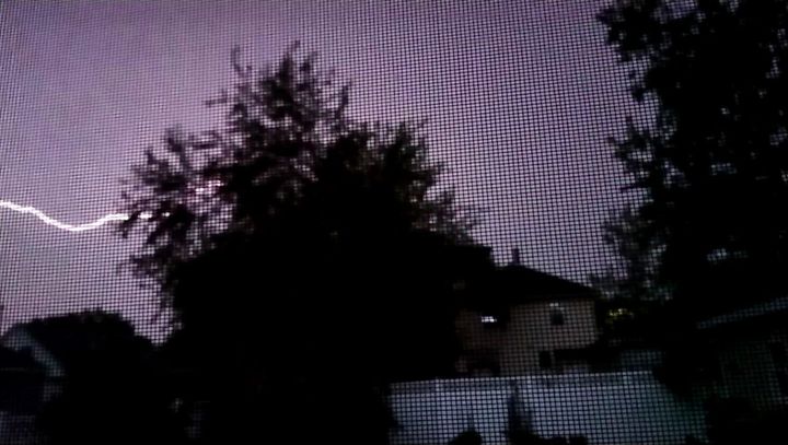 photo taken through a screen showing a lightning bolt in a purple sky with tree