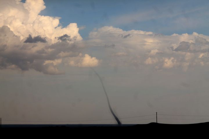 a thin landspout tornado rising into a blue and clouded sky