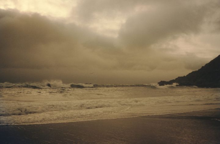 waves crashing on a beach with a headland to the right and cloudy sky