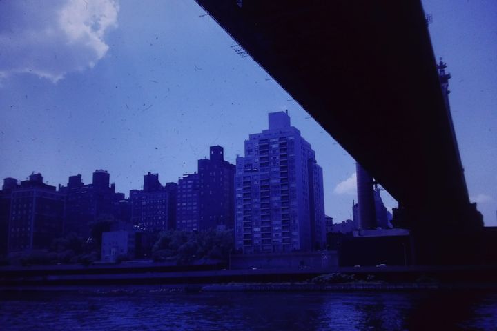 blue tinted view of buildings on the riverfront from under a bridge