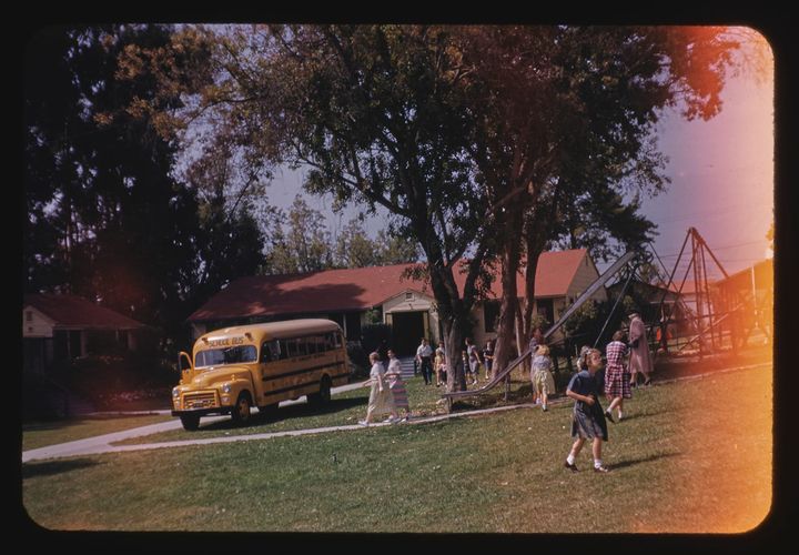 children and adults near a playground with a school bus in background