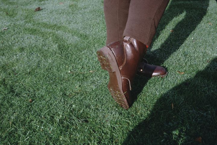 close up of a person's feet  in brown boots standing on a grass lawn