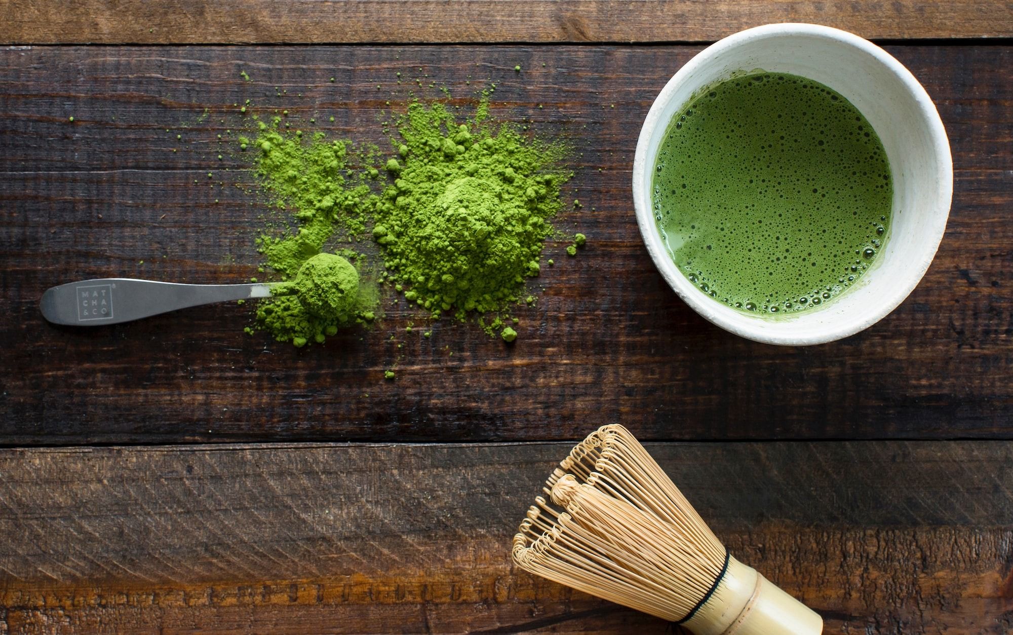 green tea powder in white ceramic mug beside brown wooden brush