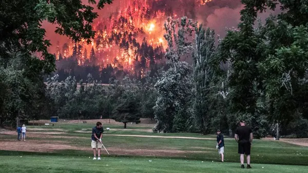 A photograph of golfers playing while a wildfire rages behind them.