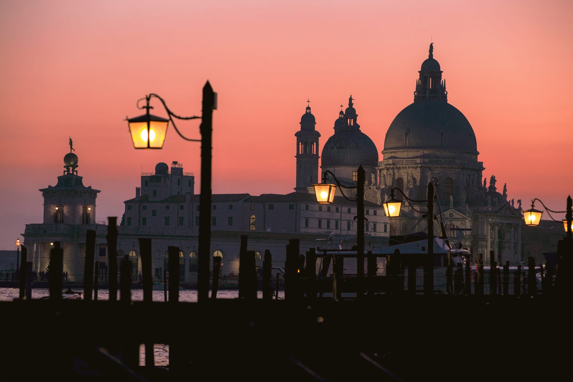 The last rays of sunshine illuminate the skyline of Venice, bathing the city in a pinkish glow.