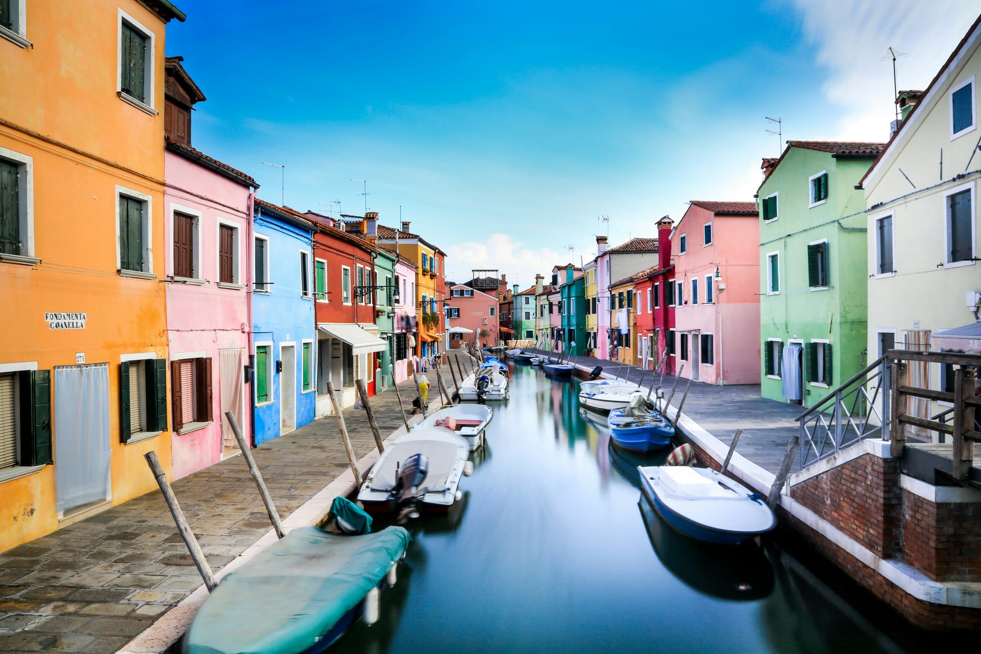 A row of brightly colored houses in blue, yellow, and red along a canal in Burano, Italy.