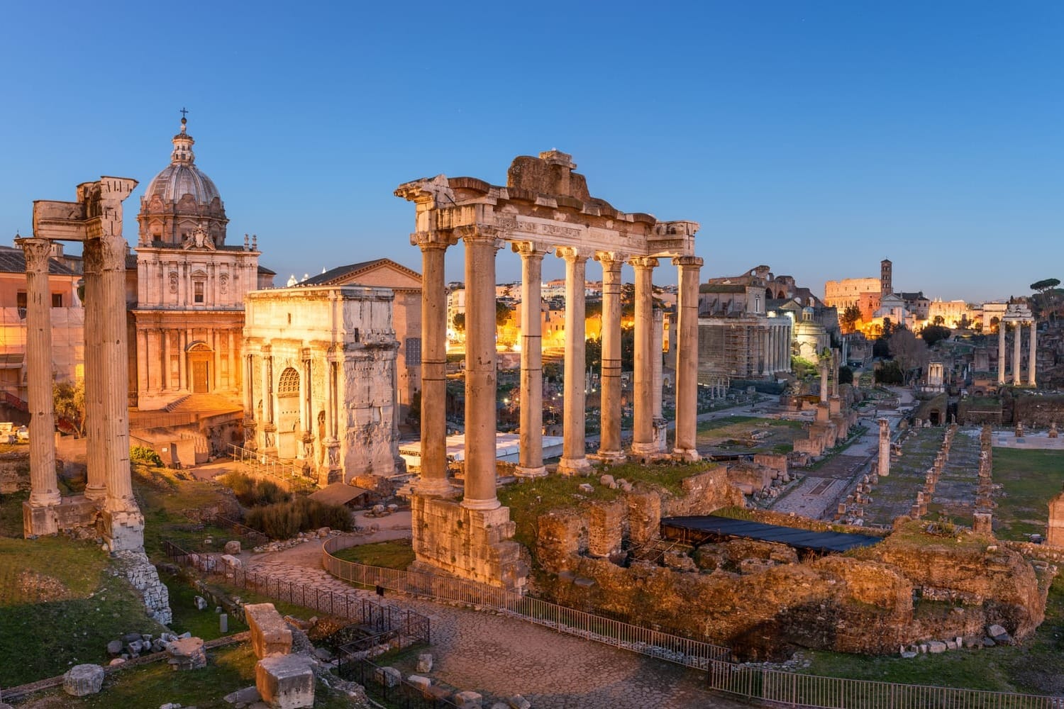 The ancient ruins of the Roman Forum in Rome, Italy, bathed in the warm, golden light of a spectacular sunset, with historic columns in the foreground.