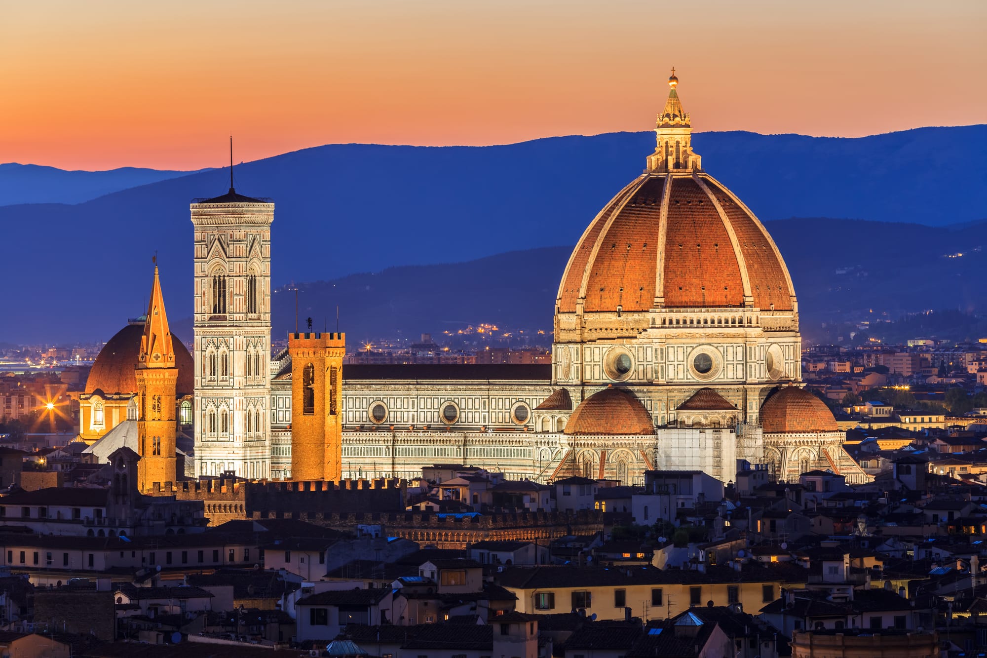 The magnificent Florence Cathedral, Santa Maria del Fiore, with Brunelleschi's iconic Duomo, stands against a vibrant sunset sky in Florence, Tuscany, Italy.