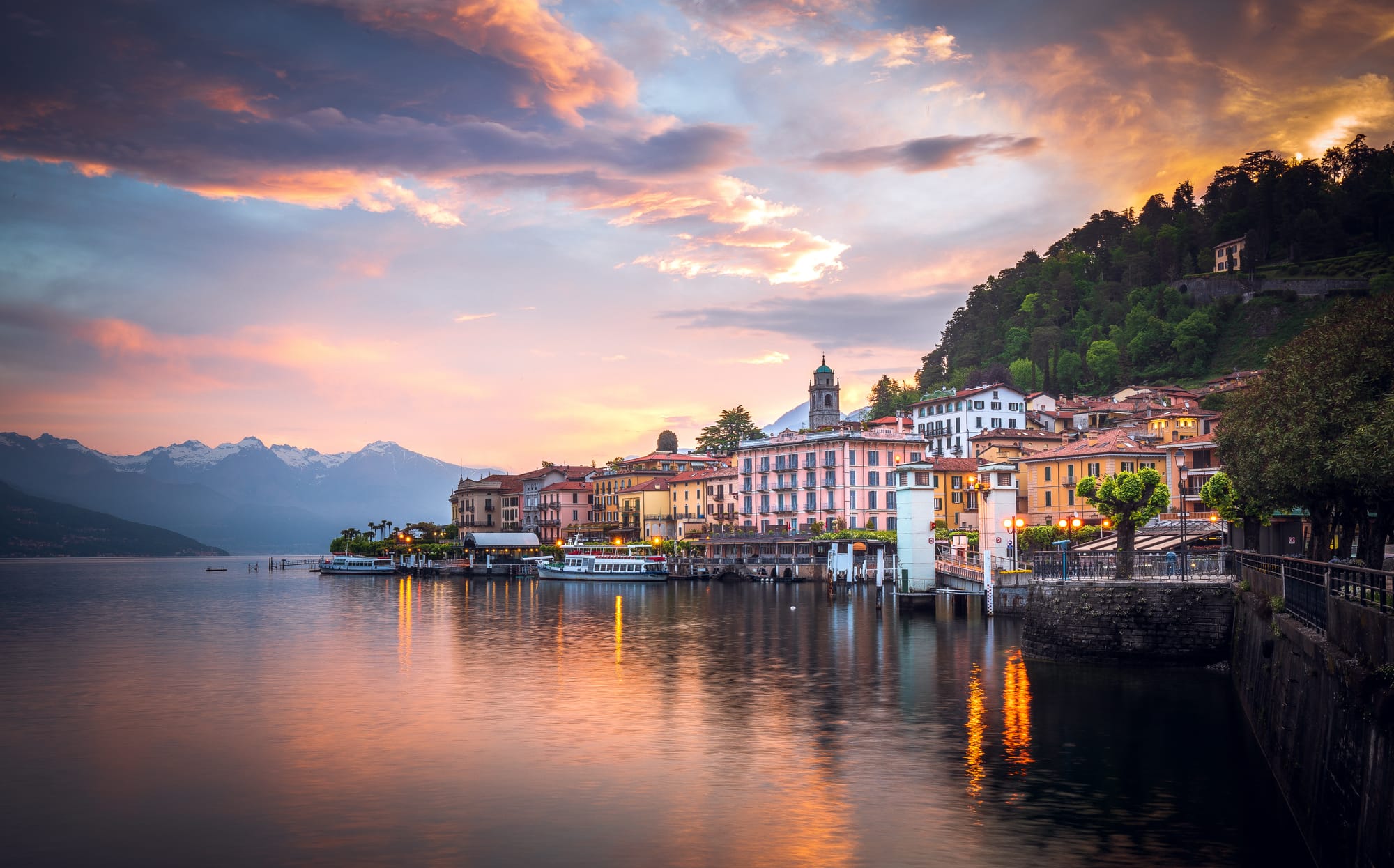 The town of Bellagio and the surrounding mountains bathed in soft pink and orange light during a romantic sunset over Lake Como.