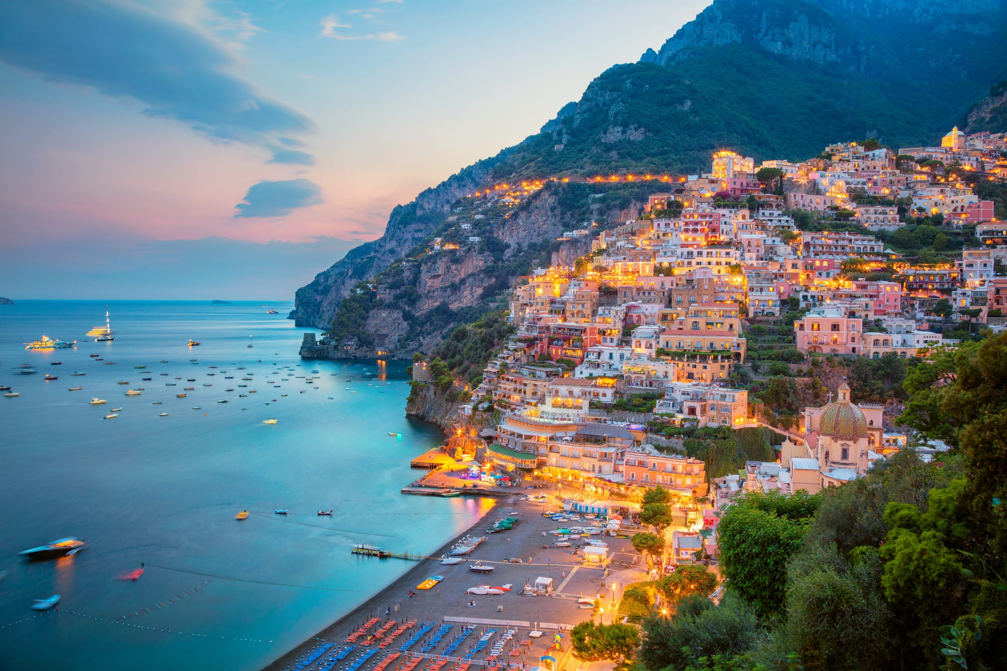Stunning aerial view of the iconic cliffside village of Positano on the Amalfi Coast, Italy, with its pastel-colored houses glowing during a beautiful sunset.