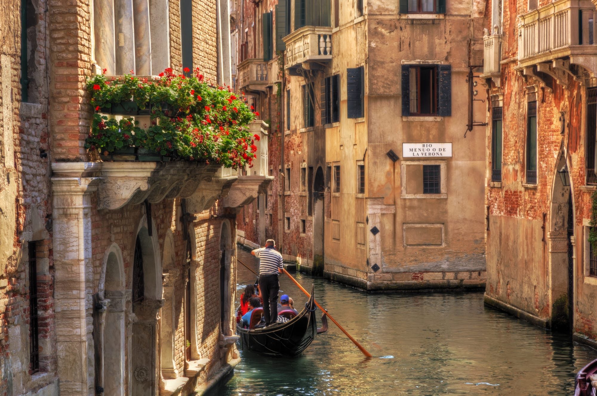 A classic black gondola navigates a narrow, romantic canal surrounded by historic buildings in Venice, Italy, reflecting the city's unique charm.