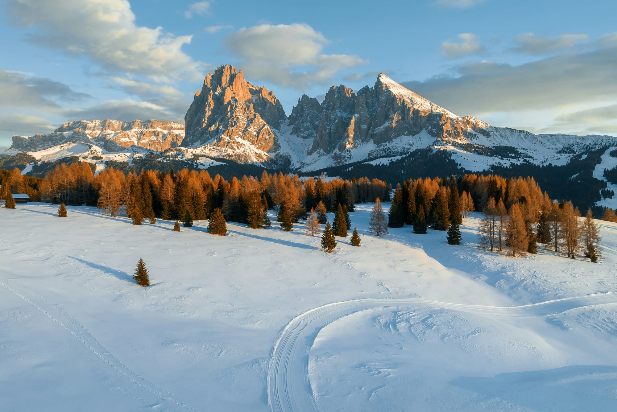 A panoramic view of the snow-covered Dolomites in winter, with jagged peaks and ski slopes under a clear blue sky