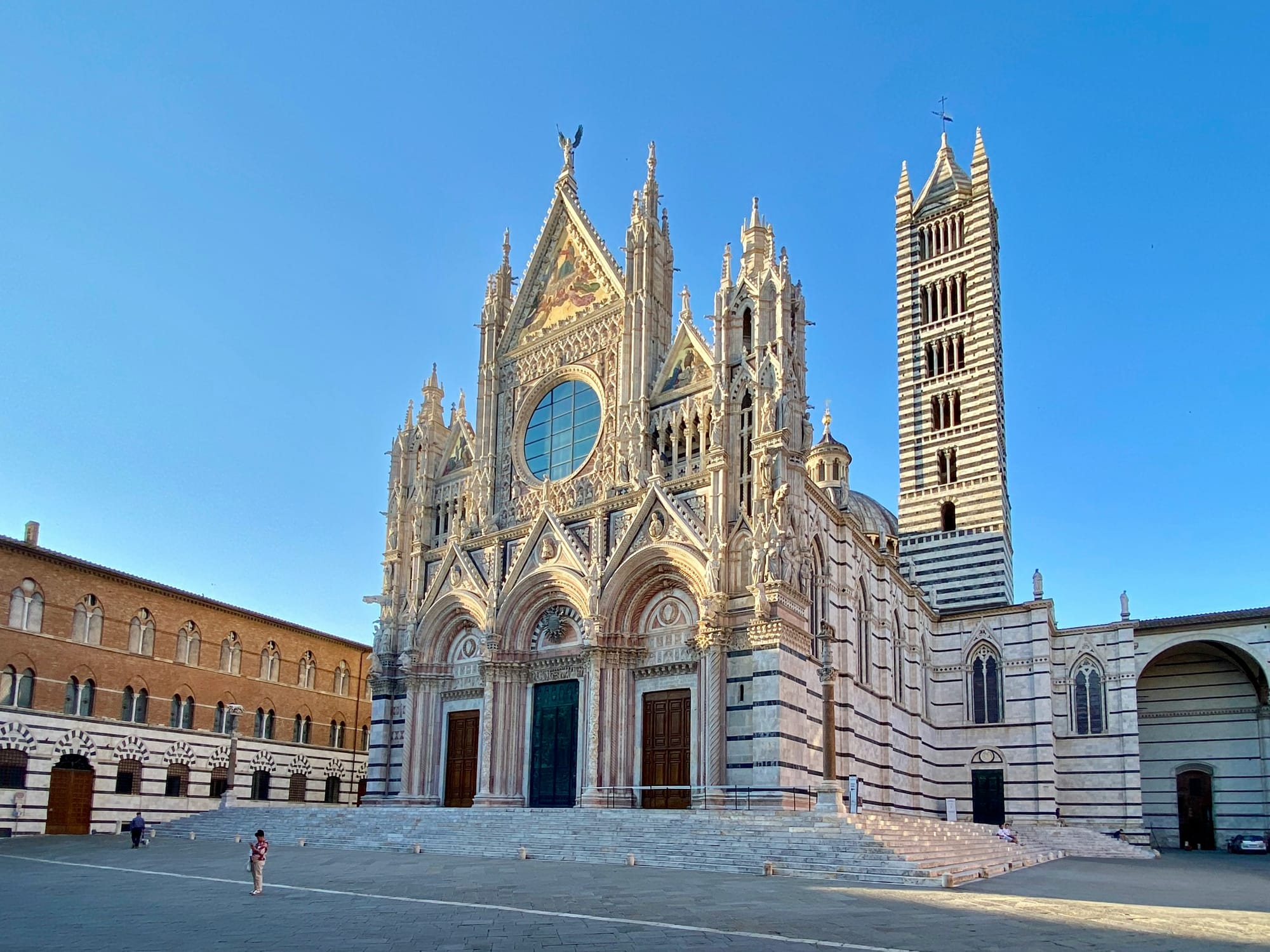 The highly detailed black, white, and red marble facade of the Duomo di Siena (Siena Cathedral) against a blue sky.
