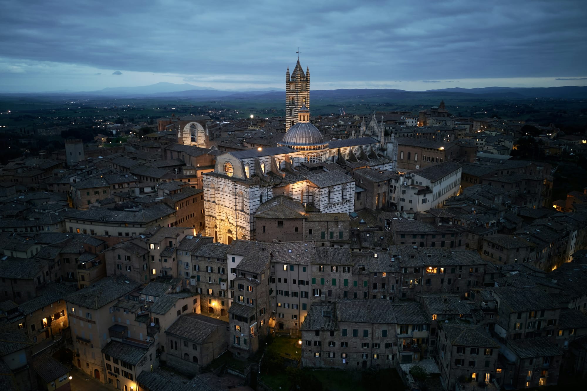 Aerial view of Siena at night, showcasing the illuminated Piazza del Campo and the medieval heart of this iconic Tuscan art city.