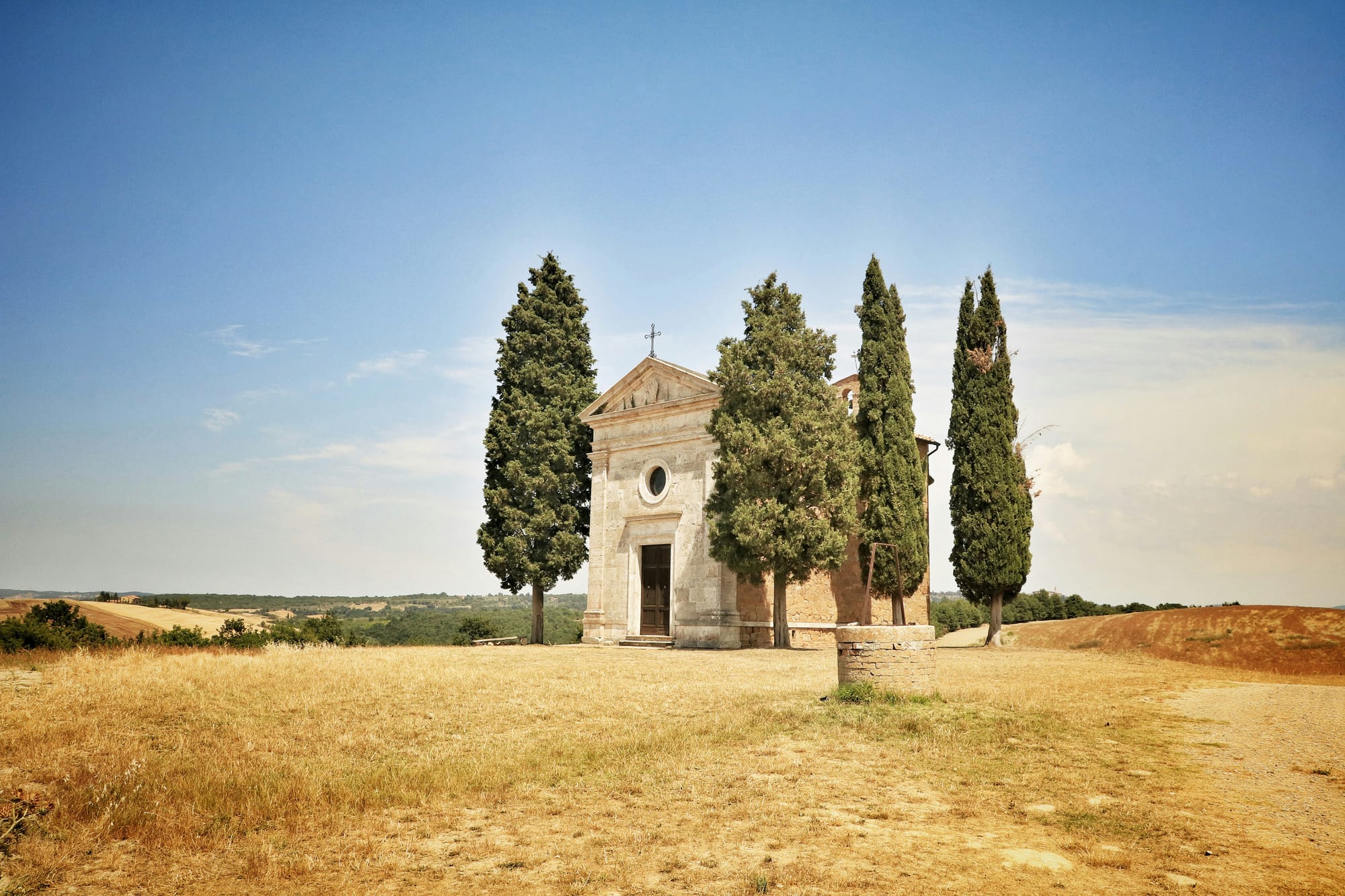 The iconic Chapel Vitaleta framed by two cypress trees in the Val d'Orcia, a famous photography spot on a Tuscany road trip.