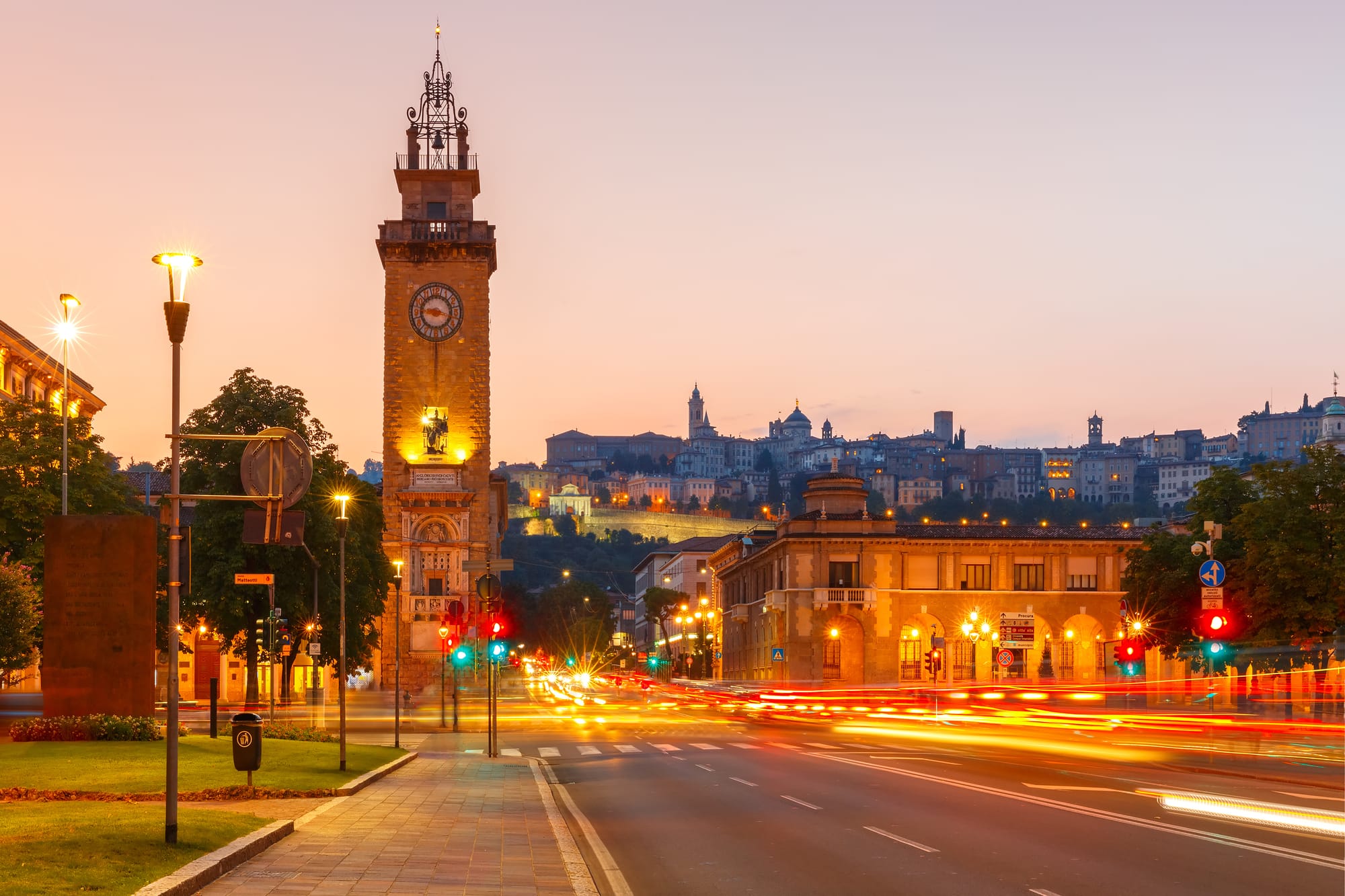 Sunset view from Porta Nuova in Bergamo's Città Bassa, looking up at the illuminated medieval Città Alta on the hill.