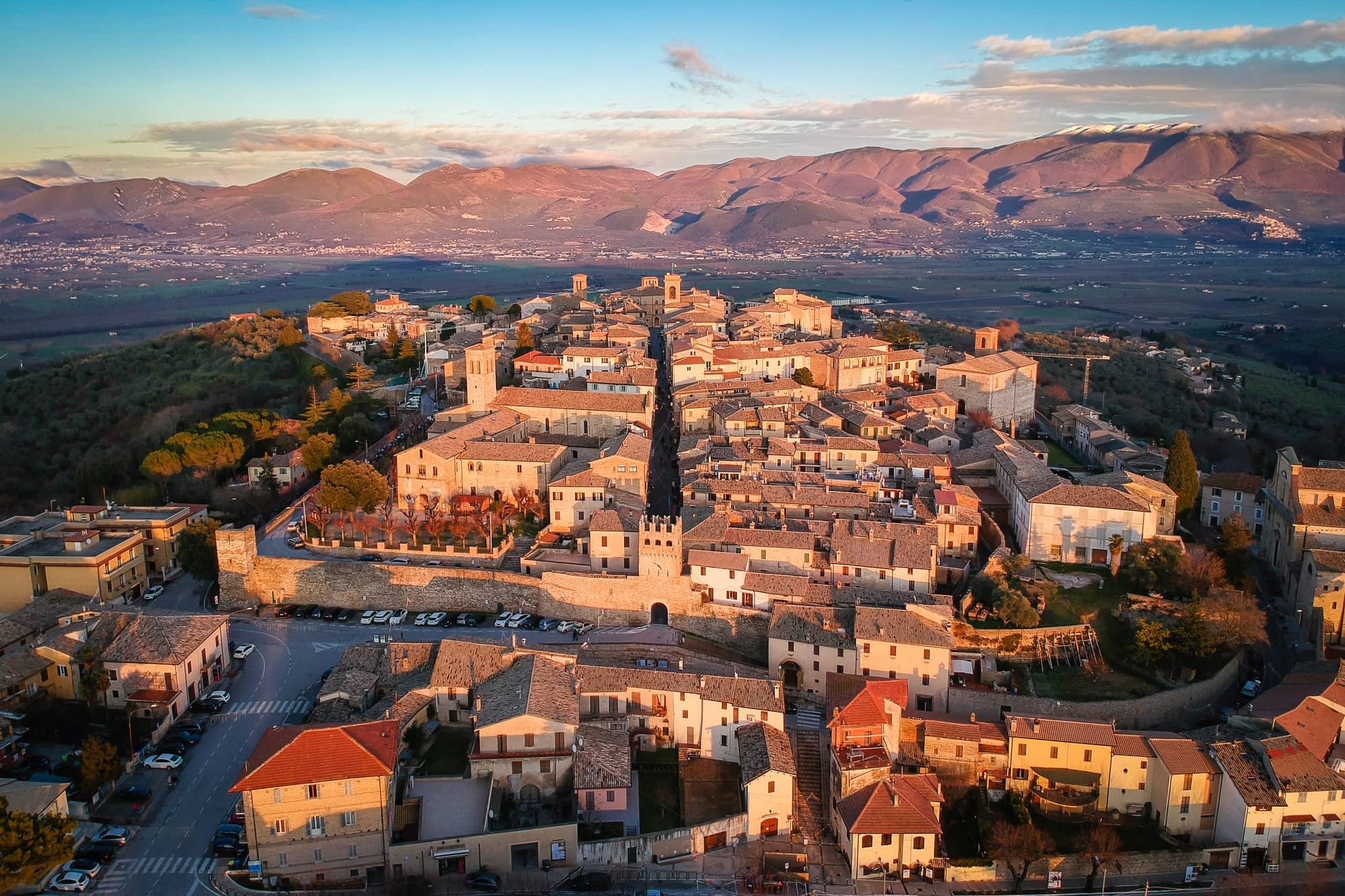 Aerial view of the historic hilltop town of Montefalco in Umbria, Italy, illuminated by the warm, golden light of an October sunset.